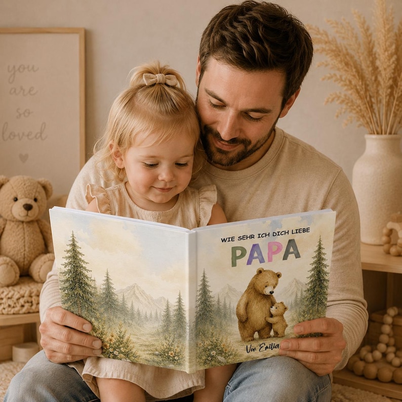 May include: A father and child are reading a book together. The book cover features a watercolor illustration of a bear and cub in a forest scene. The text on the cover reads "Wie Sehr Ich Dich Liebe Papa" and "Von Emilia".
