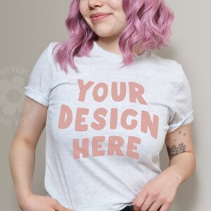 May include: A white t-shirt with the text "YOUR DESIGN HERE" in pink lettering. The shirt is being worn by a person with pink hair.