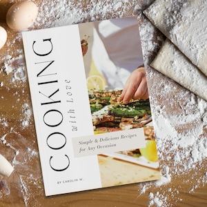 K&ouml;nnte beinhalten: Ein wei&szlig;es Kochbuch mit dem Titel "COOKING with Love" und dem Untertitel "Simple & Delicious Recipes for Any Occasion". Das Buch liegt auf einer Holzoberfl&auml;che mit verstreuter Mehl.