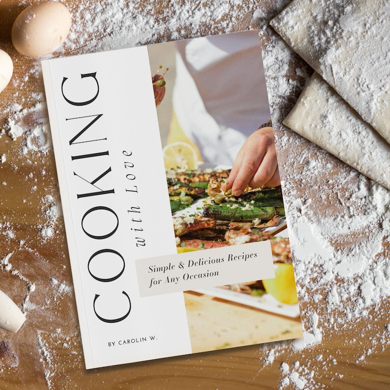 K&ouml;nnte beinhalten: Ein wei&szlig;es Kochbuch mit dem Titel "COOKING with Love" und dem Untertitel "Simple & Delicious Recipes for Any Occasion". Das Buch liegt auf einer Holzoberfl&auml;che mit verstreuter Mehl.