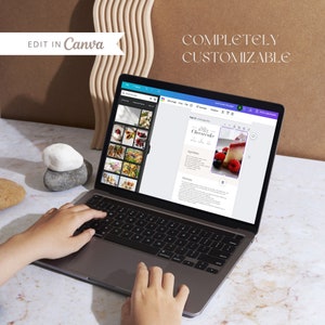 K&ouml;nnte beinhalten: Eine Person bearbeitet auf einem Laptop ein Rezept f&uuml;r No-Bake-K&auml;sekuchen. Das Rezept wird auf dem Bildschirm mit einem Foto des K&auml;sekuchens angezeigt. Der Laptop steht auf einer wei&szlig;en Oberfl&auml;che mit ein paar Steinen.
