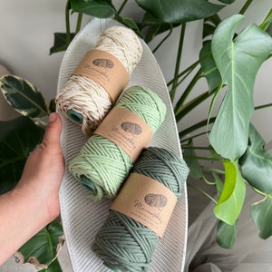 Peut inclure: Trois bobines de cordon de macramé dans une variété de couleurs, dont une couleur crème naturelle, un vert clair et un vert foncé. Les bobines sont étiquetées "Macrame Alley" et sont posées sur une assiette blanche en forme de feuille.