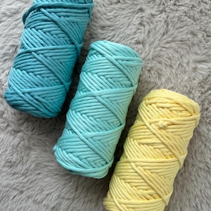 Op de afbeelding: Drie bollen garen in verschillende tinten blauw en geel. Het garen is dik en textuurrijk en perfect om te haken of te breien.