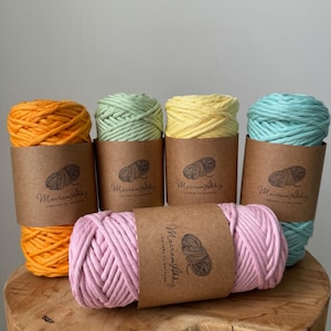 Puede incluir: Cinco carretes de cordón de algodón en varios colores, incluyendo naranja, verde, amarillo, rosa y azul claro. Cada carrete está etiquetado con "Macramé Abbaye" y "L'univers du macramé".