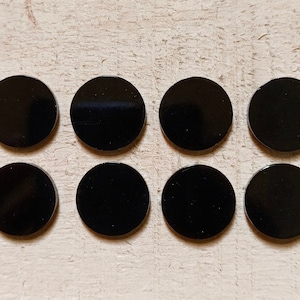 以下が含まれることがあります： 明るい木製の表面に、アメリカ合衆国の25セント硬貨と同じくらいの大きさの黒い円形のディスクが8つ、2列4つずつ並んでいます。