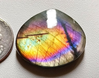 May include: A teardrop-shaped labradorite gemstone cabochon with iridescent rainbow colors, including purple, blue, green, yellow, and orange. The gemstone is approximately the size of a US quarter.