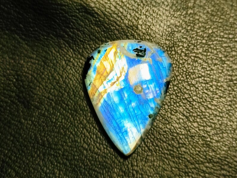 May include: A blue and gold labradorite gemstone with a unique, iridescent pattern. The gemstone is cut in a teardrop shape and has a smooth, polished surface.