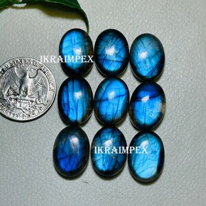 May include: Nine oval-shaped labradorite gemstones with iridescent blue and green hues. The stones are arranged in three rows of three. The text "IKRAIMPEX" appears twice in the image.