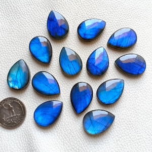 May include: A collection of 14 teardrop-shaped labradorite gemstones. The stones are a deep blue with iridescent flashes of color.