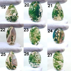 May include: A collection of nine polished moss agate gemstones in various shapes. The stones display a range of colors, including green, white, and brown, with intricate patterns resembling moss. Each stone is numbered from 19 to 27.