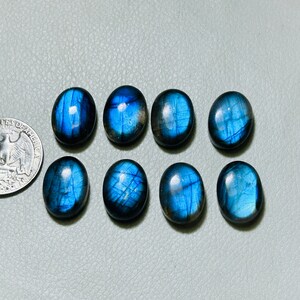 May include: Eight oval-shaped labradorite gemstones with a blue iridescent sheen. The stones are arranged in two rows of four.