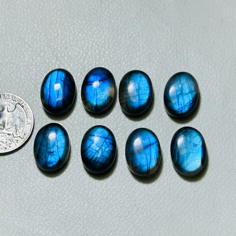 May include: Eight oval-shaped labradorite gemstones with a blue iridescent sheen. The stones are arranged in two rows of four.