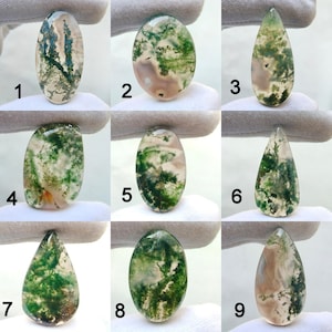 May include: Nine polished moss agate gemstones in various shapes, including oval and teardrop. The stones display green, white, and brown patterns, resembling landscapes. Each stone is unique, with variations in color and veining.