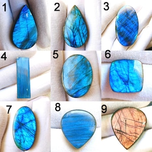 May include: Nine polished labradorite gemstones in various shapes: teardrop, oval, rectangular, and rounded. The stones display iridescent blue and teal hues with natural patterns. Each stone is unique, showcasing natural variations in color and texture.