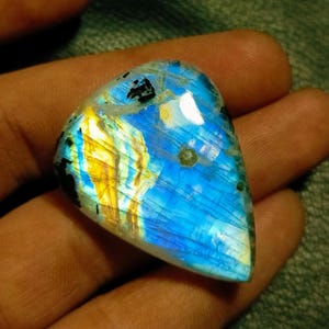 May include: A blue, gold, and white iridescent labradorite gemstone cabochon with a triangular shape.