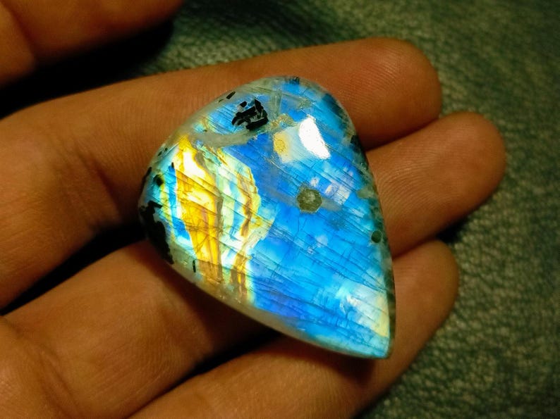 May include: A blue, gold, and white iridescent labradorite gemstone cabochon with a triangular shape.