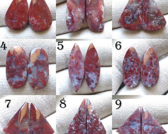 May include: Nine pairs of polished gemstones in various shapes, including teardrop, oval, and triangular. The stones display a mix of red, brown, and blue hues, with unique patterns. Each pair is presented on a white fabric background.