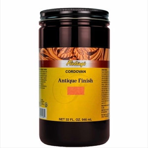 May include: A brown glass bottle with a black lid and a yellow label. The label says "Fiebing's Cordovan Antique Finish" and "Net 32 fl. oz. 946 ml".