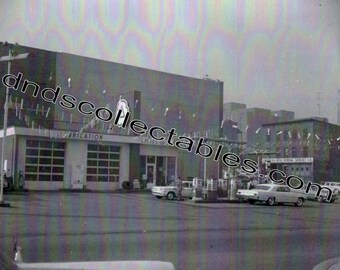 May include: A black and white photo of a gas station with a sign that reads "Oak Auto Spring Service Co.". There are several cars parked in front of the station, including a white car with a black stripe.