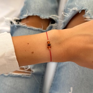 May include: A red string bracelet with three amber beads. The bracelet is worn on a person's wrist.