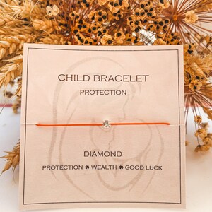 Peut inclure: Un bracelet en cordon rouge avec un petit charme en diamant. La carte indique "Bracelet enfant Protection Diamant Protection Richesse Bonne chance".