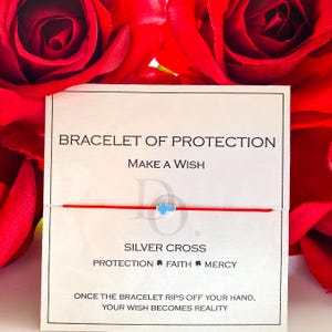 Può includere: Un braccialetto di filo rosso con un ciondolo a croce argentata, presentato su una carta bianca. La carta recita "Braccialetto di protezione" e "Esprimi un desiderio". Lo sfondo presenta rose rosse.