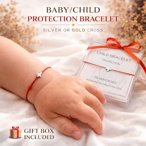 Puede incluir: Una pulsera roja con un dije de cruz plateada en la muñeca de un bebé. La imagen incluye una caja de regalo y texto que dice "PULSERA DE PROTECCIÓN PARA BEBÉ/NIÑO" y "CRUZ DE PLATA O ORO". La pulsera está empaquetada en una caja transparente con una cinta roja.