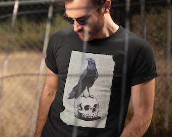 May include: A black t-shirt with a graphic print of a raven perched on a skull. The raven is black with blue accents and the skull is white.