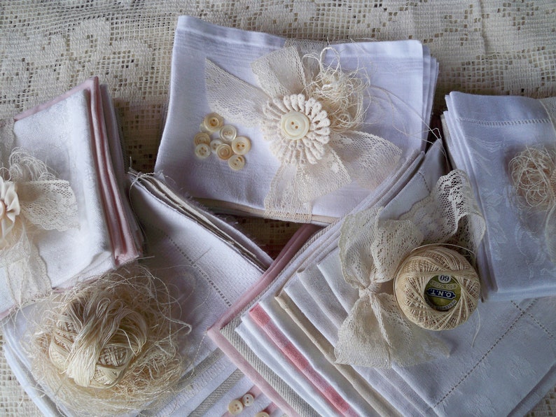 May include: A collection of white and pink-trimmed handkerchiefs, adorned with lace, buttons, and thread. Some handkerchiefs are embellished with lace bows and floral accents, creating a vintage aesthetic. The arrangement suggests a craft or textile theme.