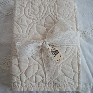 May include: A white quilted journal with a lace ribbon tied around it. The journal has a vintage look and feel.