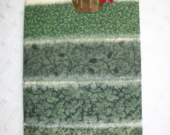 May include: Four strips of green fabric with different patterns, including leaves and swirls. The fabric is trimmed with white fringe. A small gold pumpkin with red and brown leaves is attached to the top of the fabric.