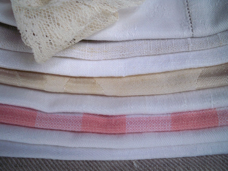 May include: A stack of folded white and cream-colored linens, including a lace-trimmed piece. Various textures are visible, such as linen, cotton, and a gingham pattern in pink and white. The fabrics are neatly arranged, suggesting a home decor or textile theme.