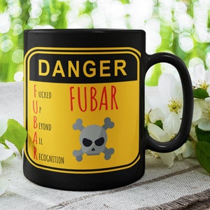 Puede incluir: Taza de café negra con una señal de advertencia amarilla que dice "Danger FUBAR" con una calavera y huesos cruzados y el acrónimo escrito como "F*cked Up Beyond All Recognition".