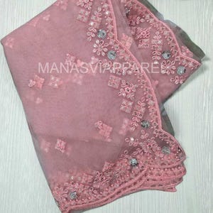 May include: A light pink sheer saree with intricate floral embroidery and sequin embellishments. The saree features a delicate border and the text "MANASVIAPPAREL". This elegant garment is suitable for special occasions.