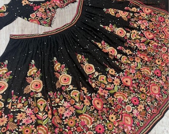 May include: A black embroidered lehenga choli set. The skirt and blouse are adorned with colorful floral embroidery in shades of pink, orange, and green. The set includes a matching dupatta.