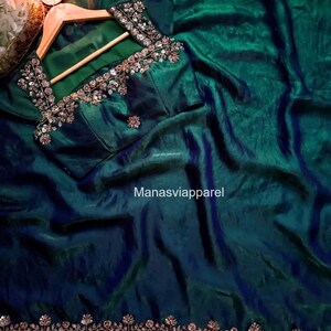 May include: A teal green saree and blouse set. The blouse is embellished with silver and gold embroidery around the neckline and sleeves. The saree has a shimmering, textured finish. The text "Manasviapparel" is visible.