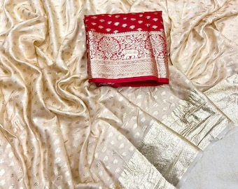 Peut inclure: Un sari en soie de couleur crème avec une bordure dorée et un pallu rouge et or. Le pallu présente un motif traditionnel avec des éléphants et des motifs floraux.