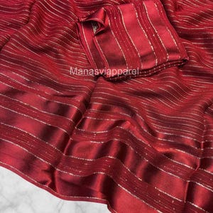 May include: A deep red fabric with horizontal silver stripes. The fabric is draped, with a matching folded square of fabric on top. The text "Manasviapparel" is visible on the fabric.