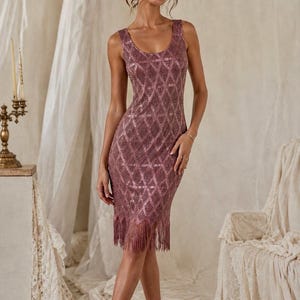 May include: A knee-length sleeveless dress in a dusty rose hue, featuring a prominent diamond-shaped lattice pattern throughout the fabric and a delicate fringe trim along the bottom hemline, finished with a simple scoop neckline.