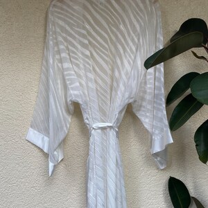 May include: White satin robe with a zebra print pattern. The robe has long sleeves and a tie belt.