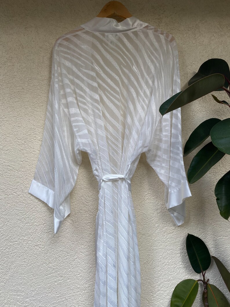 May include: White satin robe with a zebra print pattern. The robe has long sleeves and a tie belt.