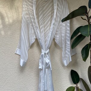 May include: White satin robe with a zebra print pattern. The robe has a tie belt and long sleeves.