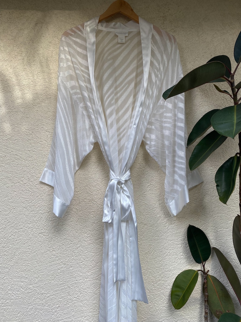 May include: White satin robe with a zebra print pattern. The robe has a tie belt and long sleeves.