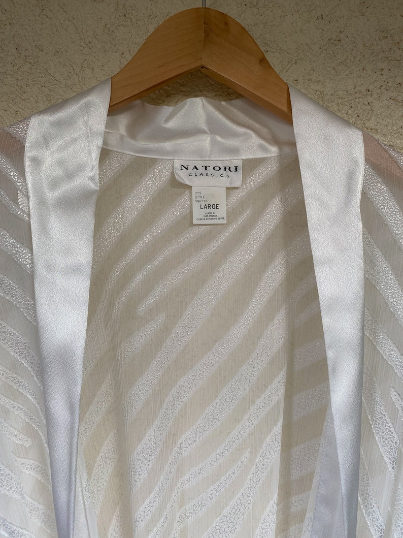 May include: White satin robe with a zebra print pattern. The robe has a satin collar and a tie closure. The label reads "Natori Classics" and "Large".