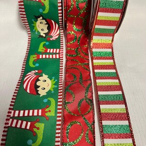 May include: Three decorative Christmas ribbons. One green ribbon features elf faces and legs. A red ribbon has a glittery green swirl pattern. The third ribbon has red, green, and white horizontal stripes.