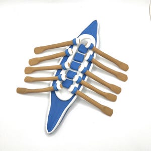 May include: A miniature rowing boat made of clay, painted blue and white with eight brown oars. This is a decorative item.