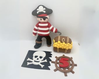 May include: A red and white striped pirate figurine with a black eyepatch and a black hat with a white skull and crossbones. The pirate is holding a hook and standing next to a brown treasure chest with gold coins. There is also a black pirate flag with a white skull and crossbones and a brown wooden steering wheel with a red number 5.