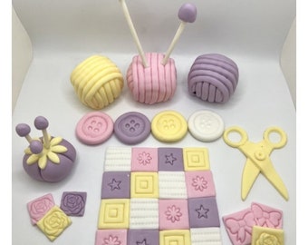 Könnte beinhalten: Ein Set aus violetten, rosa und gelben Fondant-Kuchen-Toppern mit Wollknäueln, Knöpfen, einem Nadelkissen, einem Patchwork-Deckenstück und einer Schere. Diese Topper sind perfekt für einen Kuchen zum Thema Nähen.