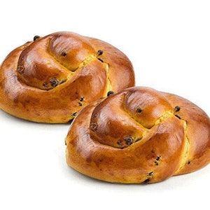 May include: Two golden-brown, baked bread rolls with a spiral design. The rolls have a glossy finish and are dotted with dark raisins. The background is plain white, highlighting the baked goods.