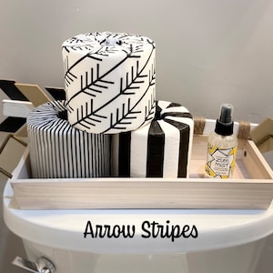 May include: A wooden tray with black and white striped toilet paper rolls and a bottle of Zum Mist room spray. The tray is sitting on a white toilet tank with the words "Arrow Stripes" written on the front.